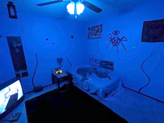 a barren blue room with a CRT and a black sigil painted on the wall